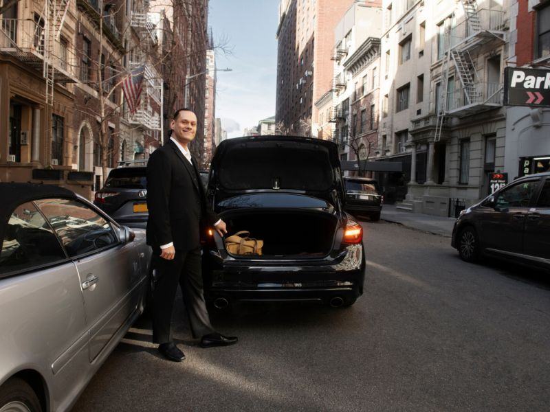 A well-dressed man stands next to a luxury car, exuding professionalism and style.