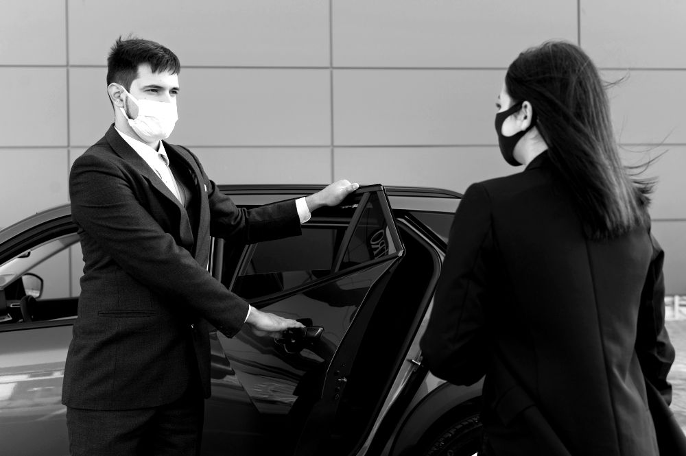A man and woman dressed in business attire are getting into a car, indicating a work-related journey.