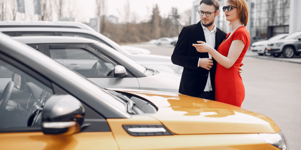 A man and woman pose next to a car, both looking happy and relaxed in a casual outdoor setting.