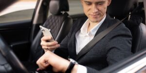A suited man is engaged with his phone while driving, illustrating the risks of distracted driving.