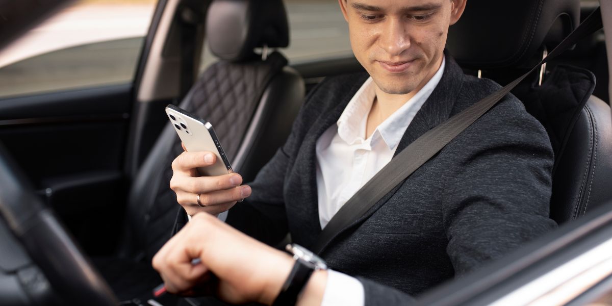 A suited man is engaged with his phone while driving, illustrating the risks of distracted driving.