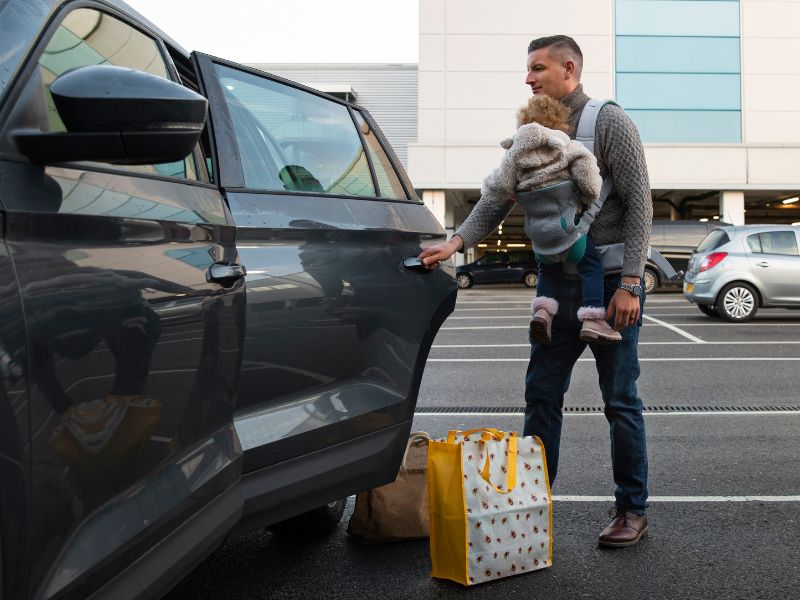 A man and a child are standing next to a car, sharing a joyful moment in a sunny outdoor setting.