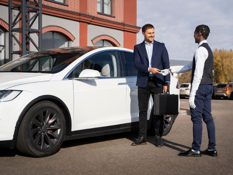 Two men engaged in a handshake beside a white Tesla car, indicating a successful negotiation or collaboration.