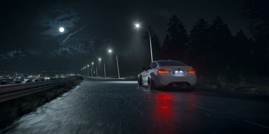 White sports car driving away on a wet, dark, tree-lined road under a full moon and streetlights