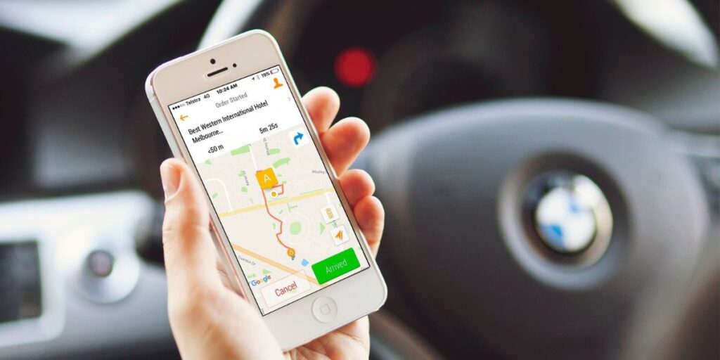 A person holding a smartphone showing a ride-hailing app with a map and directions inside a car
