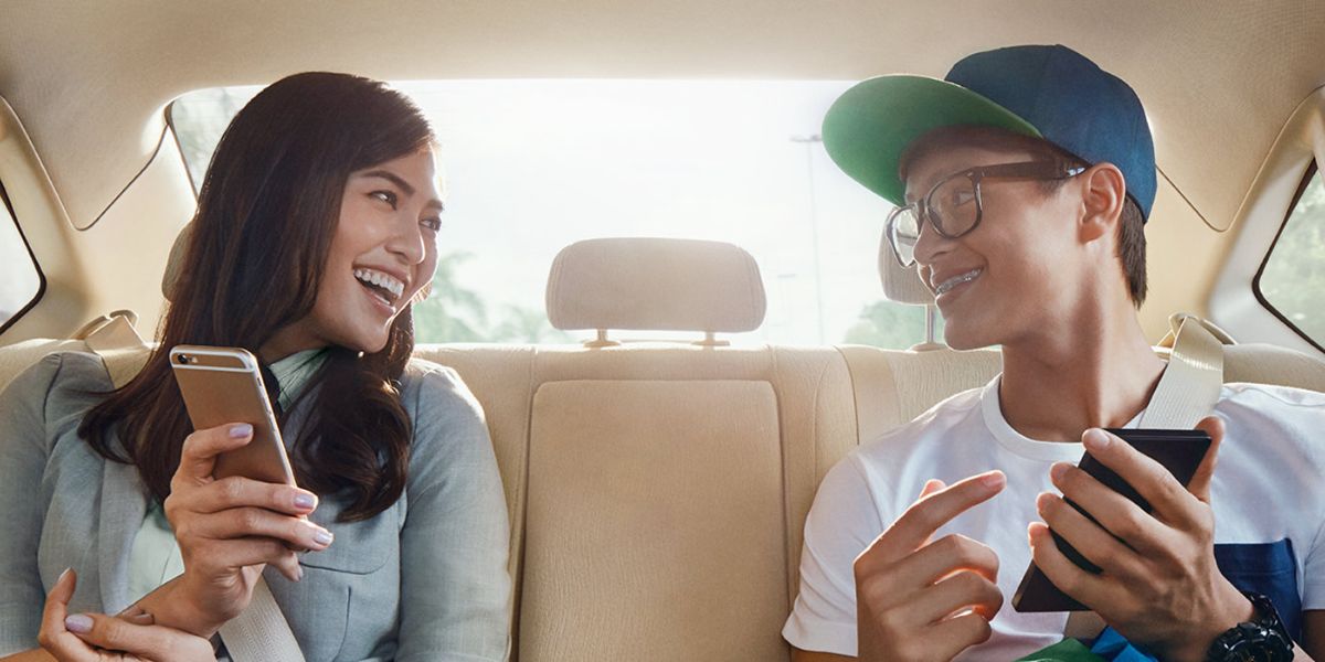 A man and woman sit in a car's back seat, both focused on their cell phones.
