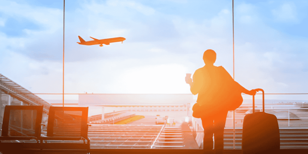A silhouette of a traveler with luggage standing in an airport, suggesting movement and anticipation of departure.