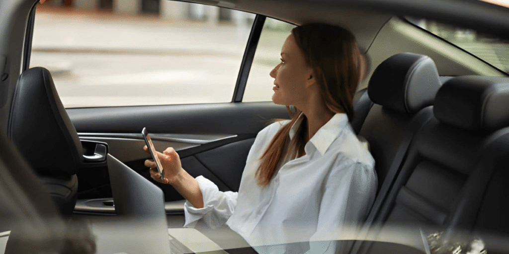 A woman in the back seat of a car, focused on her cell phone while seated comfortably.
