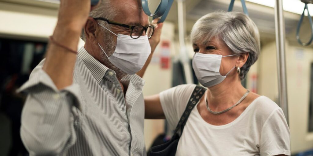 An elderly man and woman wearing protective face masks while standing and holding onto handrails inside a subway car