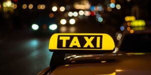 A glowing yellow taxi sign on a car roof at night with blurred city lights and traffic bokeh in the background.