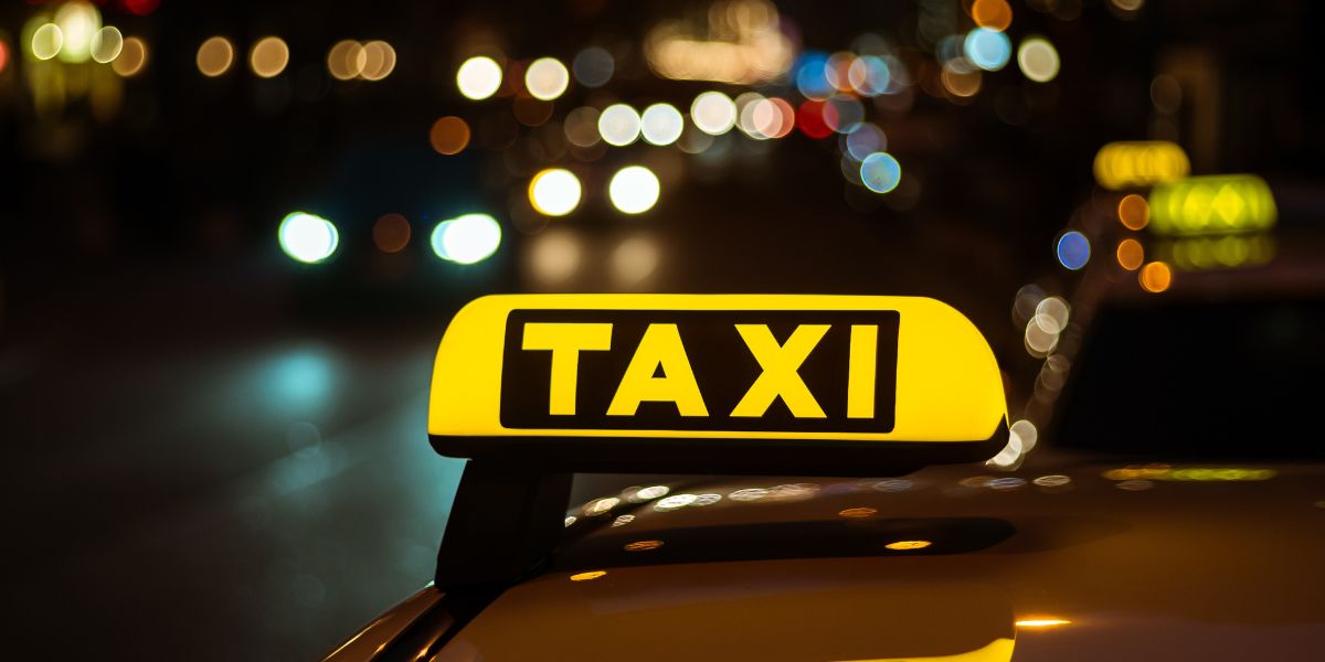 A glowing yellow taxi sign on a car roof at night with blurred city lights and traffic bokeh in the background.